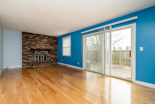 unfurnished living room with a textured ceiling, a brick fireplace, and light hardwood / wood-style flooring