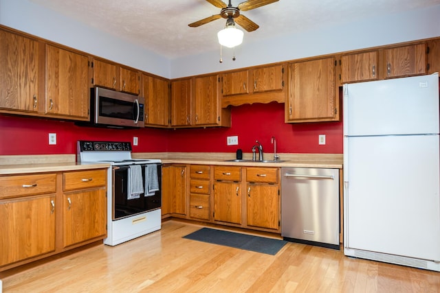 kitchen featuring appliances with stainless steel finishes, sink, light wood-type flooring, ceiling fan, and a textured ceiling