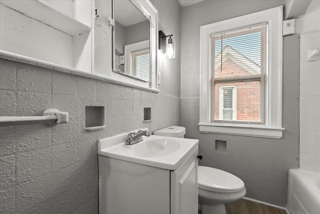 bathroom with wood-type flooring, tile walls, vanity, toilet, and a bath