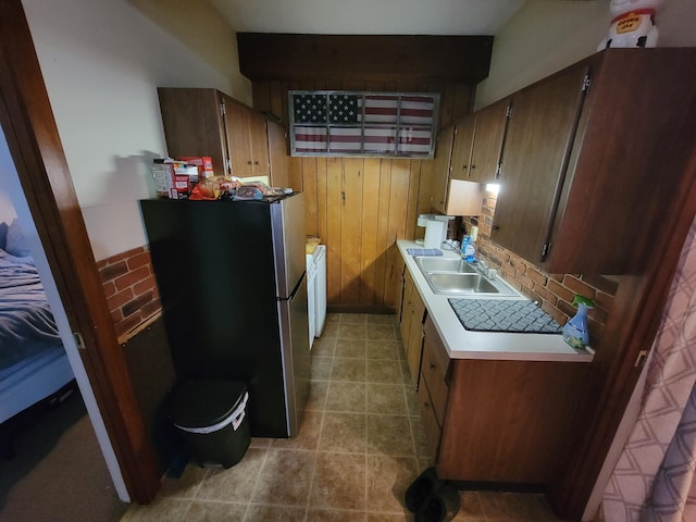 kitchen featuring light tile patterned flooring, stainless steel refrigerator, wood walls, washer / dryer, and sink