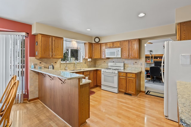 kitchen featuring sink, white appliances, a kitchen breakfast bar, light hardwood / wood-style floors, and kitchen peninsula