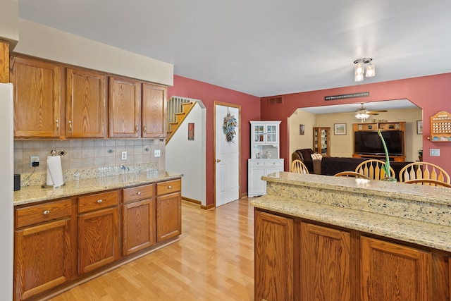 kitchen featuring tasteful backsplash, ceiling fan, light stone counters, and light hardwood / wood-style flooring