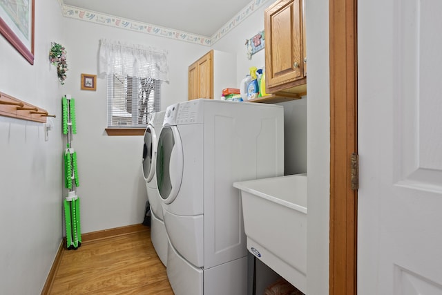 laundry area featuring cabinets, separate washer and dryer, sink, and light wood-type flooring