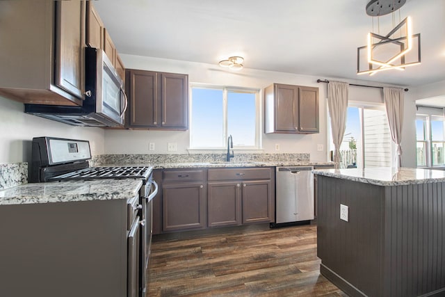 kitchen featuring sink, dark wood-type flooring, appliances with stainless steel finishes, light stone countertops, and decorative light fixtures