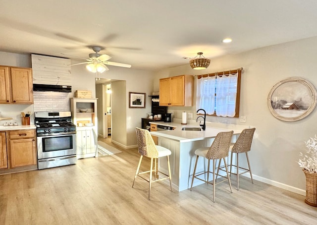 kitchen with a breakfast bar area, stainless steel range with gas stovetop, sink, light wood-type flooring, and kitchen peninsula