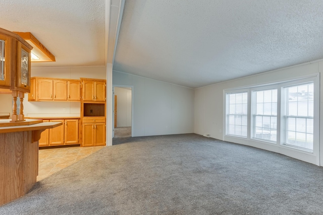 unfurnished living room with light colored carpet, lofted ceiling with beams, and a textured ceiling