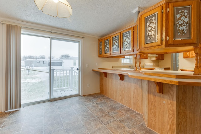 kitchen with a breakfast bar area, range, a textured ceiling, and kitchen peninsula