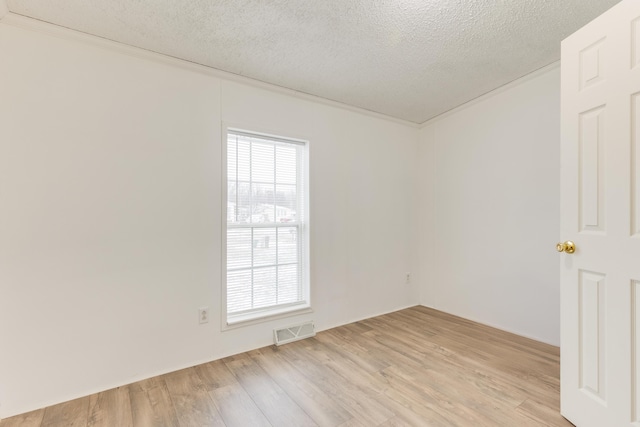 empty room featuring a wealth of natural light, a textured ceiling, and light wood-type flooring