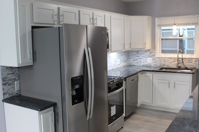 kitchen with white cabinetry, sink, dark stone counters, stainless steel appliances, and light hardwood / wood-style flooring