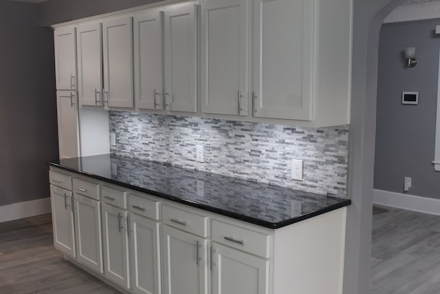 kitchen featuring tasteful backsplash, white cabinets, light hardwood / wood-style floors, and dark stone counters