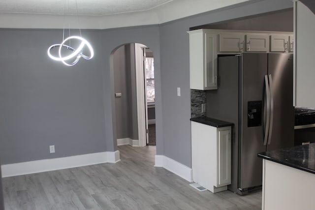 kitchen with pendant lighting, stainless steel fridge with ice dispenser, tasteful backsplash, and white cabinets