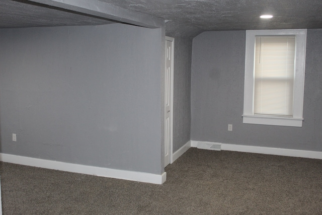 basement featuring a textured ceiling and dark colored carpet