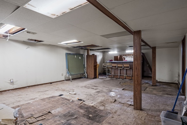 basement featuring a paneled ceiling and bar