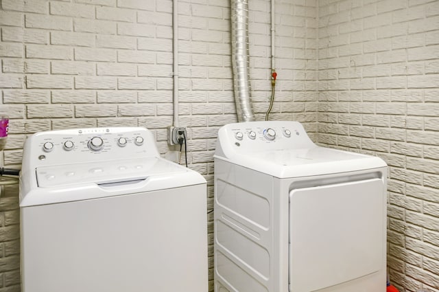 clothes washing area featuring brick wall and washer and dryer