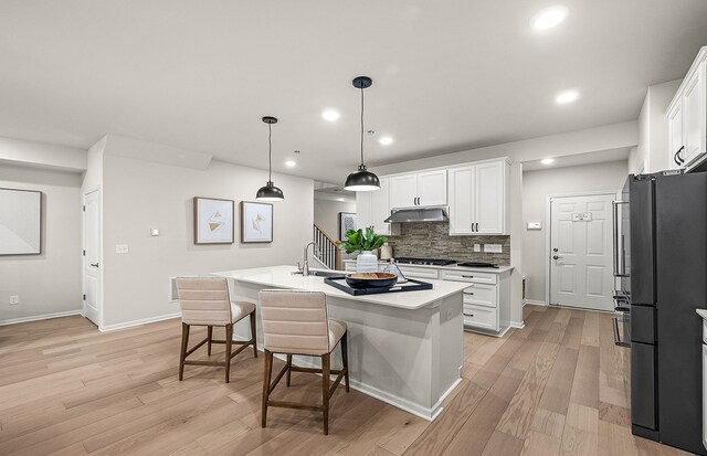 kitchen featuring freestanding refrigerator, white cabinets, tasteful backsplash, and under cabinet range hood