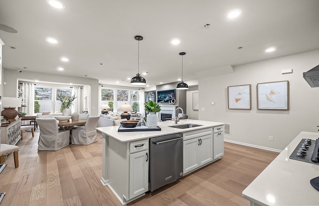kitchen featuring open floor plan, stainless steel dishwasher, a sink, light wood-style flooring, and a kitchen island with sink
