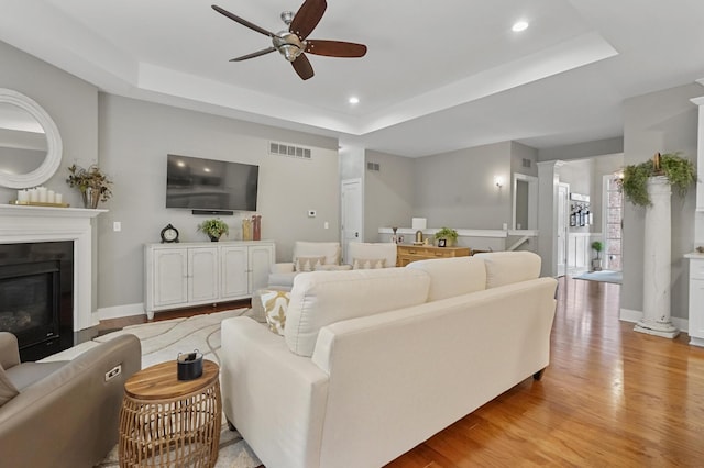 living room featuring a tray ceiling, decorative columns, ceiling fan, and light wood-type flooring