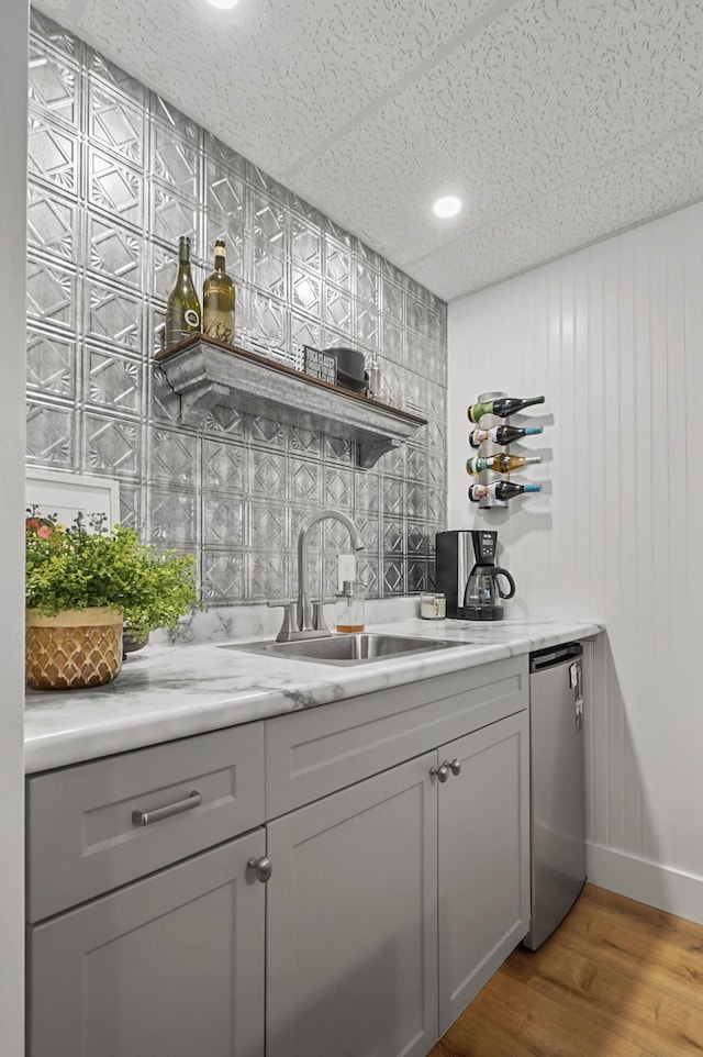 bar featuring sink, a paneled ceiling, dishwasher, gray cabinetry, and light hardwood / wood-style floors