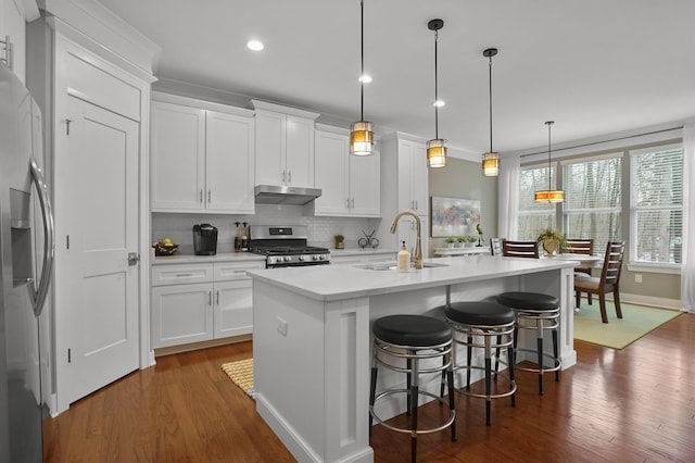 kitchen with a kitchen bar, appliances with stainless steel finishes, an island with sink, pendant lighting, and white cabinets