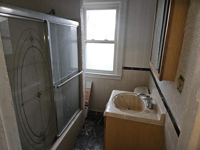 bathroom with enclosed tub / shower combo, vanity, and tile walls