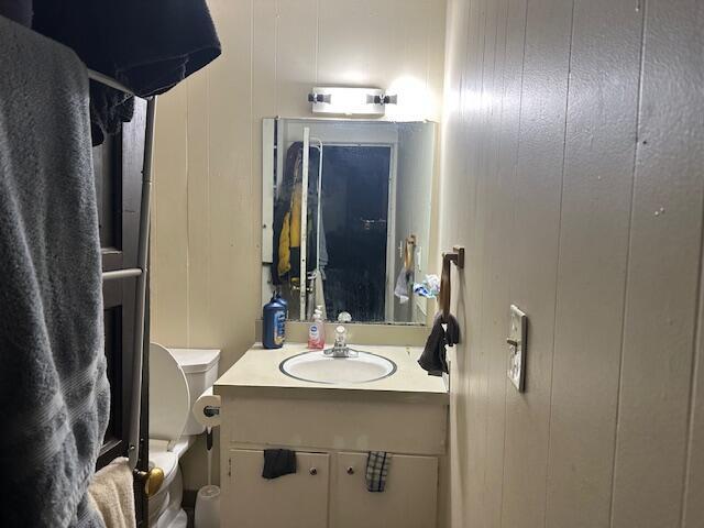 bathroom with vanity, wooden walls, and toilet