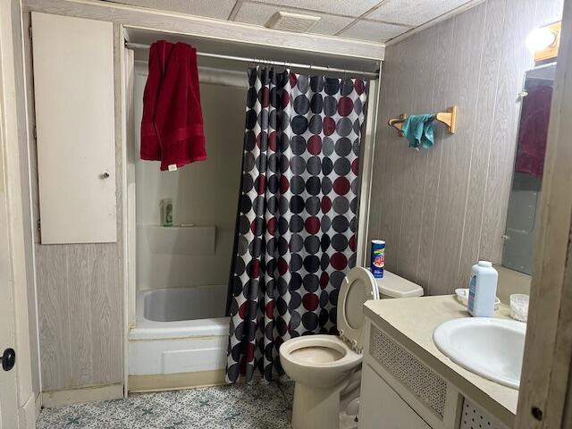 full bathroom with shower / tub combo with curtain, toilet, vanity, wooden walls, and a drop ceiling