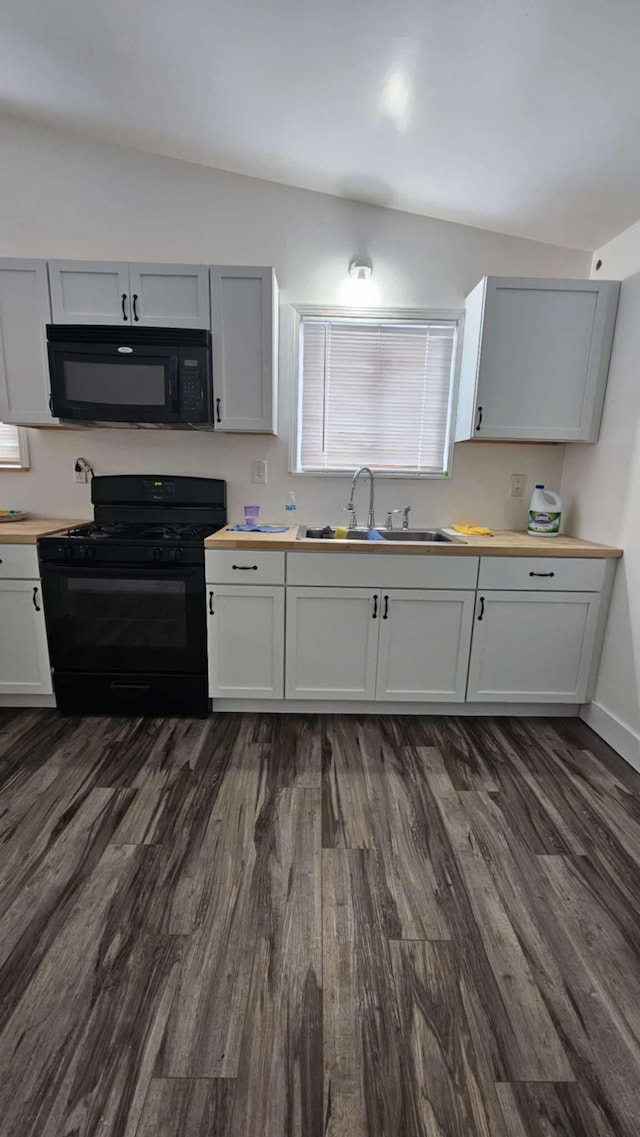 kitchen featuring dark wood-type flooring, lofted ceiling, sink, white cabinetry, and black appliances