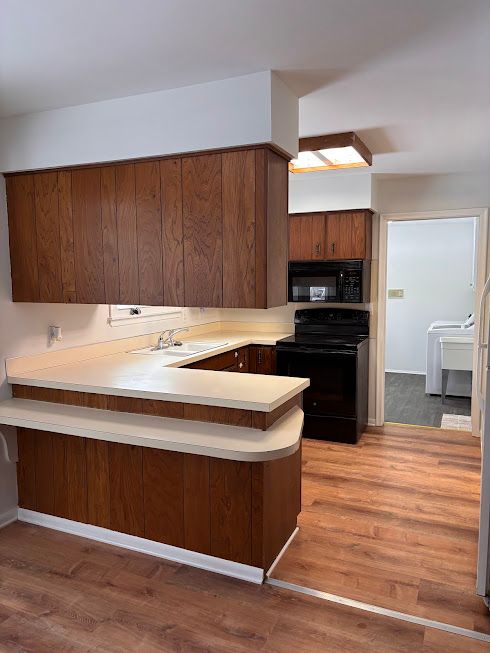 kitchen featuring sink, black appliances, dark hardwood / wood-style flooring, washer / dryer, and kitchen peninsula