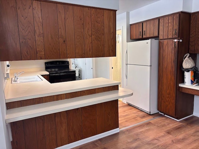 kitchen with kitchen peninsula, sink, white fridge, and electric range