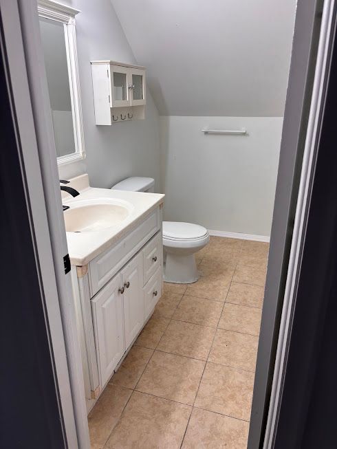 bathroom with lofted ceiling, vanity, tile patterned floors, and toilet