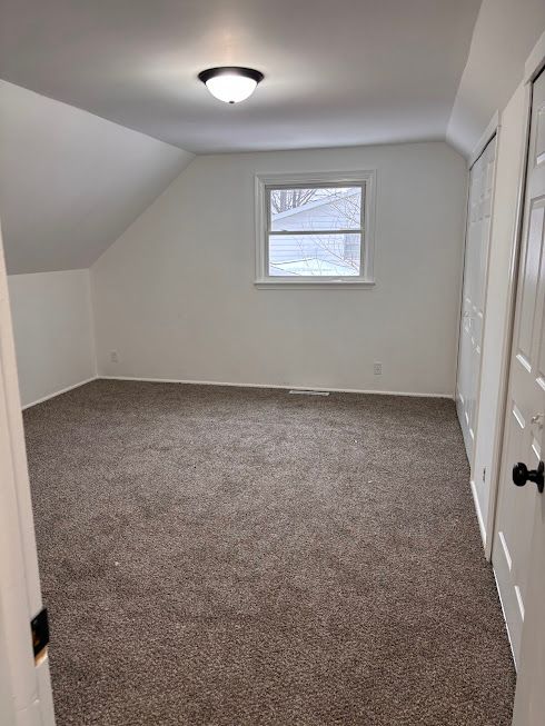 additional living space featuring lofted ceiling and dark colored carpet