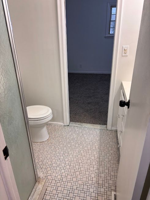 bathroom featuring an enclosed shower, tile patterned flooring, and toilet