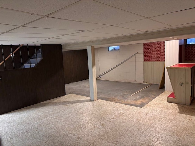 basement with a drop ceiling and wooden walls