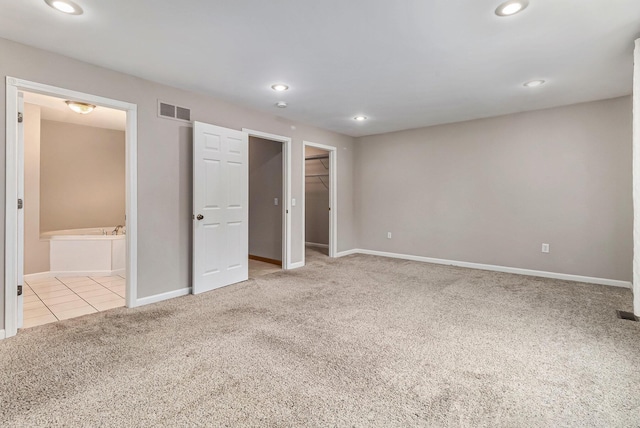 unfurnished bedroom with light carpet, connected bathroom, a spacious closet, and a closet