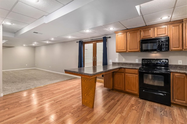 kitchen featuring a kitchen bar, light hardwood / wood-style flooring, black appliances, and a paneled ceiling