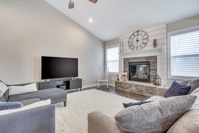 living room with hardwood / wood-style flooring, a stone fireplace, high vaulted ceiling, and ceiling fan