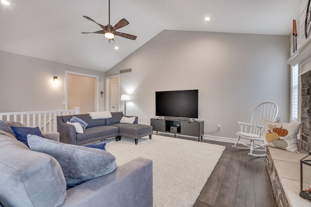 living room featuring a stone fireplace, dark wood-type flooring, high vaulted ceiling, and ceiling fan