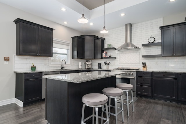 kitchen featuring a kitchen island, appliances with stainless steel finishes, pendant lighting, a breakfast bar area, and wall chimney exhaust hood