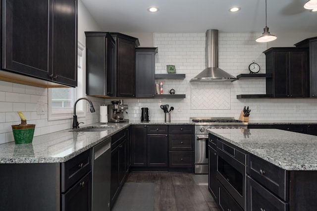 kitchen with sink, dark wood-type flooring, appliances with stainless steel finishes, hanging light fixtures, and wall chimney exhaust hood