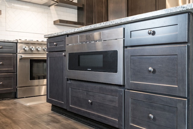 kitchen featuring dark wood-type flooring, backsplash, wall oven, light stone countertops, and stainless steel range oven