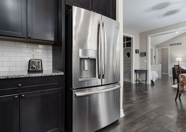 kitchen with tasteful backsplash, lofted ceiling, light stone counters, stainless steel refrigerator with ice dispenser, and dark wood-type flooring