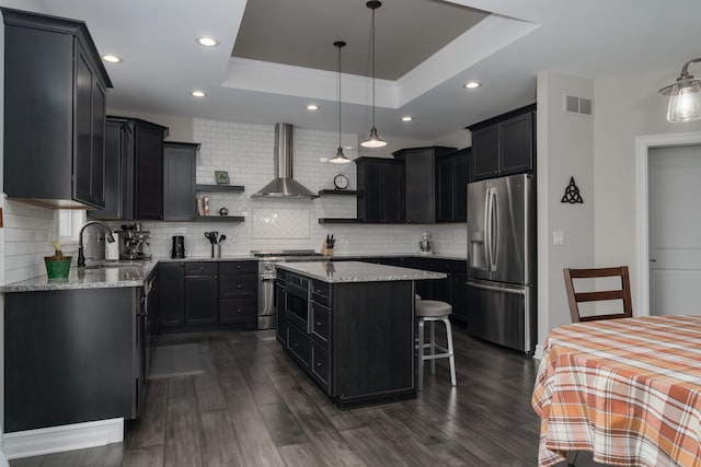 kitchen featuring a kitchen island, appliances with stainless steel finishes, dark hardwood / wood-style floors, a tray ceiling, and wall chimney exhaust hood