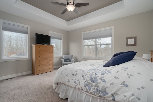 carpeted bedroom with ceiling fan and a tray ceiling