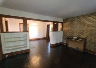 unfurnished living room featuring brick wall and dark hardwood / wood-style floors