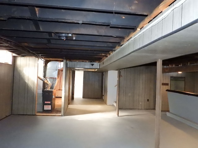 basement featuring wooden walls and heating unit