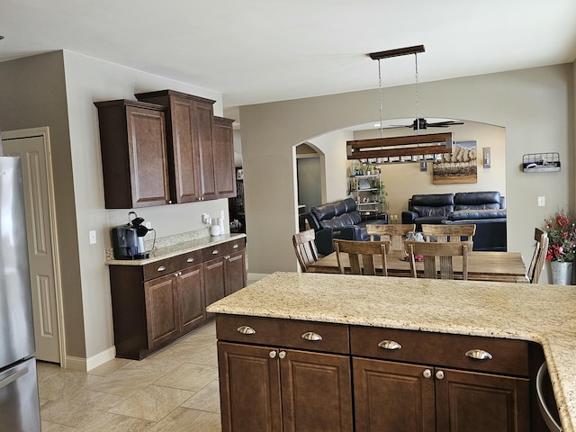 kitchen with dark brown cabinets, stainless steel fridge, light stone counters, and decorative light fixtures