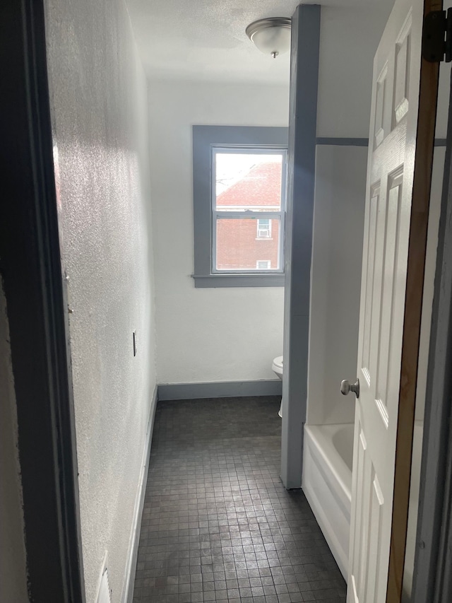 bathroom with tile patterned flooring, a tub to relax in, and toilet