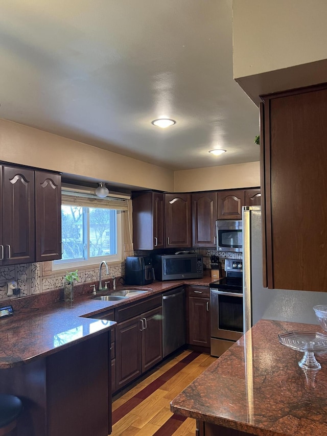 kitchen with sink, backsplash, stainless steel appliances, dark brown cabinetry, and light hardwood / wood-style floors