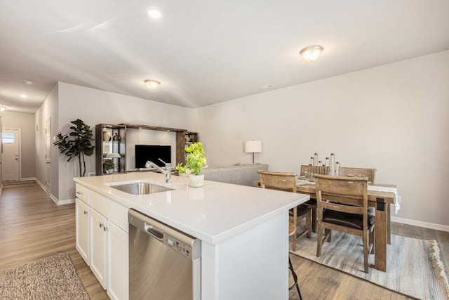 kitchen featuring an island with sink, sink, white cabinets, stainless steel dishwasher, and light hardwood / wood-style flooring