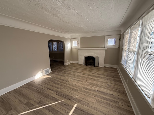 unfurnished living room featuring visible vents, a textured ceiling, wood finished floors, arched walkways, and a brick fireplace